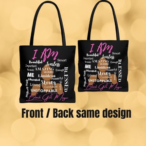 May include: Black tote bag featuring a design of brown skin tone words that say "I AM" with pink words such as "fearless", "amazing", "limitless", "strong", "unstoppable", and "Black Girl Magic". The bag has black handles and a black canvas.