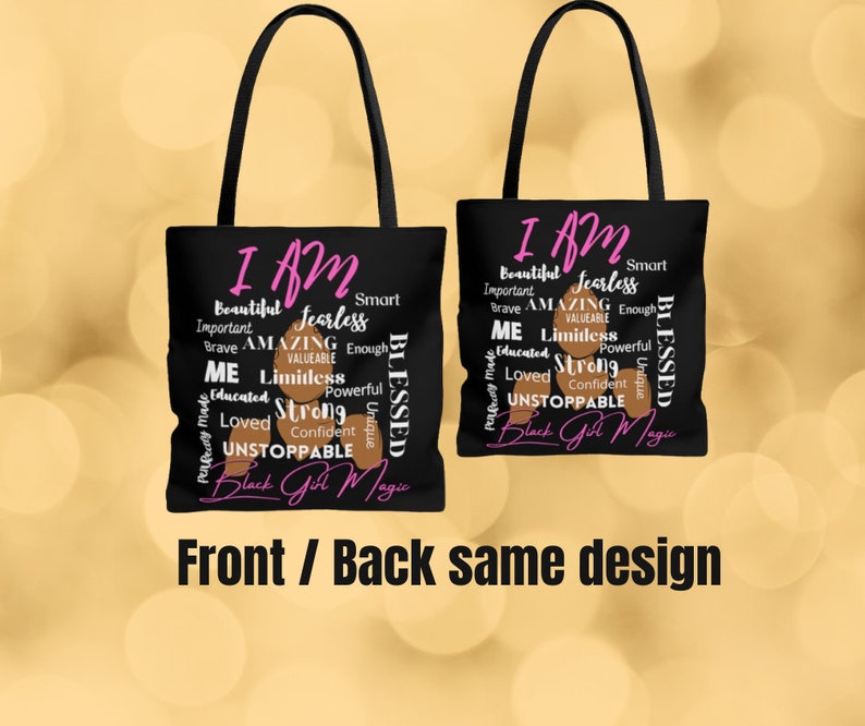 May include: Black tote bag featuring a design of brown skin tone words that say "I AM" with pink words such as "fearless", "amazing", "limitless", "strong", "unstoppable", and "Black Girl Magic". The bag has black handles and a black canvas.