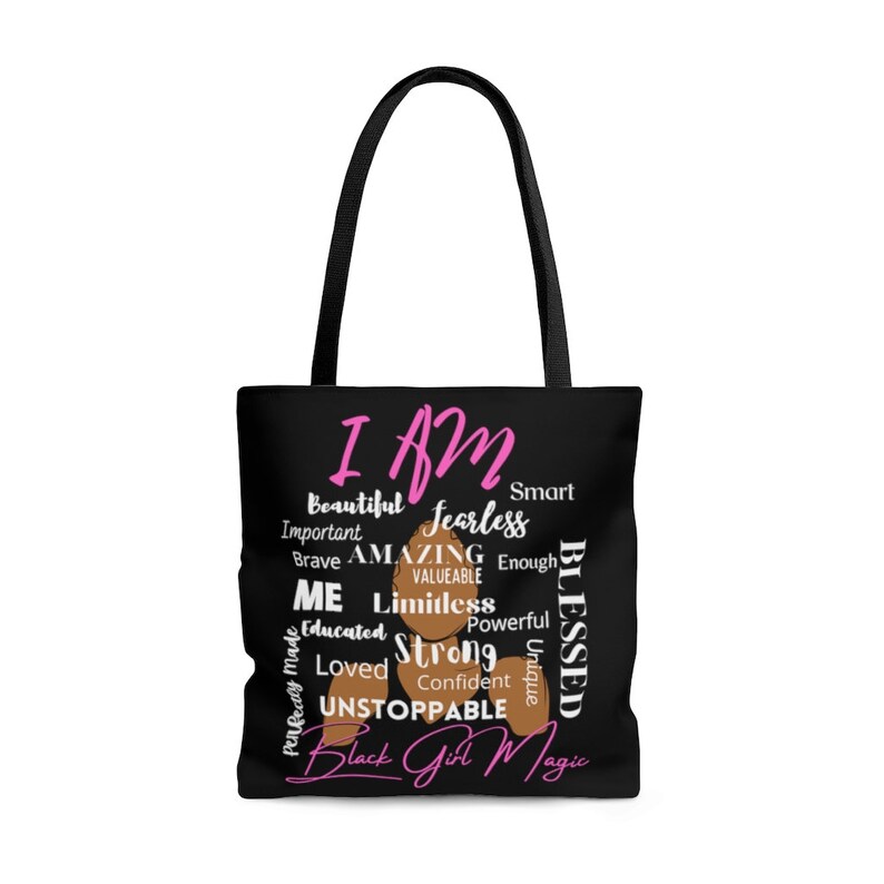 May include: Black tote bag featuring a black and brown illustration of a woman's head. The text "I AM" is in large pink letters. The words "Beautiful, Fearless, Amazing, Blessed, Limitless, Strong, Unstoppable, Black Girl Magic" are written around the illustration in pink letters.