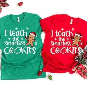 May include: Two green and red t-shirts with a gingerbread man graphic and the text "I teach the smartest cookies" on each shirt.