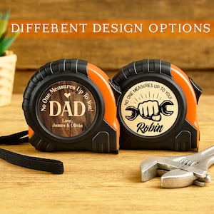May include: Two orange and black tape measures with personalized designs. One features "DAD" with a heart and the names "James & Olivia." The other has a wrench graphic and the name "Robin." The text "No One Measures Up To You" is on both. A silver wrench is also present.