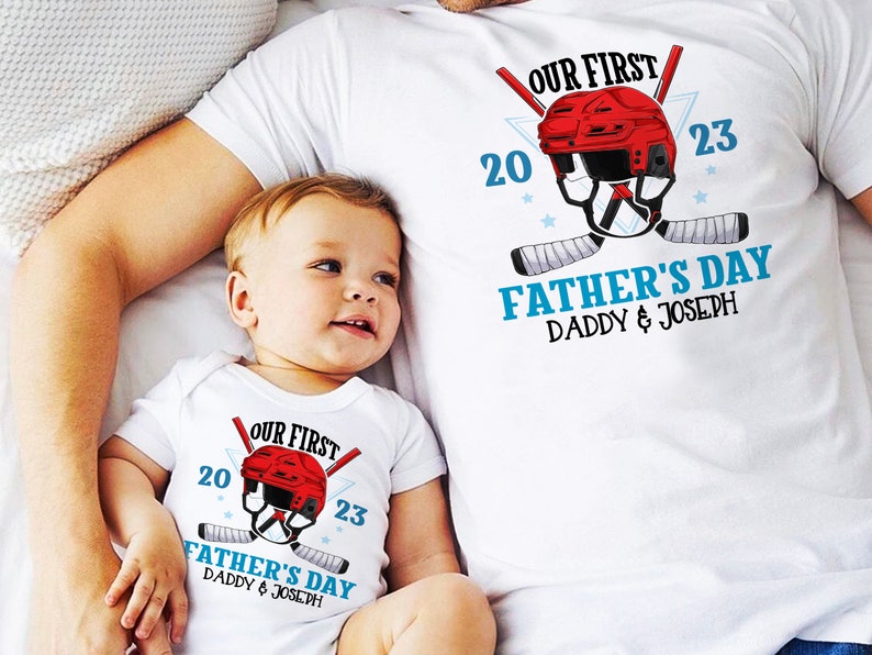 May include: A white t-shirt with a red hockey helmet graphic and the text "Our First Father's Day Daddy & Joseph 20 23". A white onesie with the same graphic and text is worn by a baby.