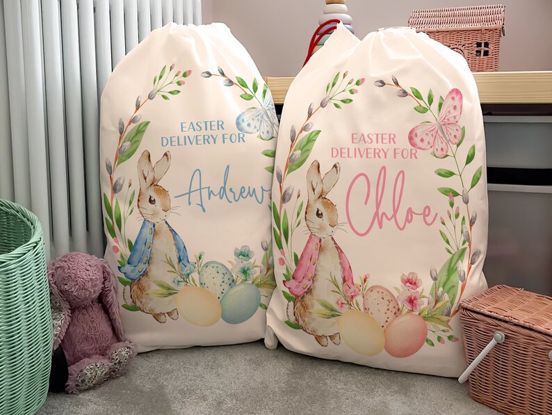 Pu&ograve; includere: Due sacchetti regalo di Pasqua in tela bianca con nomi personalizzati. Il sacchetto a sinistra ha un coniglio blu con uova blu e il testo "Easter Delivery for Andrew". Il sacchetto a destra ha un coniglio rosa con uova rosa e il testo "Easter Delivery for Chloe".