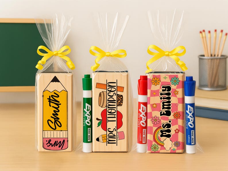 K&ouml;nnte beinhalten: Drei Geschenksets f&uuml;r Lehrer, jeweils mit einem personalisierten Holzblock und einem Whiteboard-Marker. Ein Block zeigt ein Bleistift-Design mit "Smith" und "Mrs.". Die anderen Bl&ouml;cke haben "Mrs. Thompson" und "Ms. Emily" mit Schulmotiven.