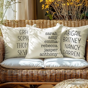 May include: Three white throw pillows with black text on a wicker couch. The pillows have the names "GRACE, SOPH, THOM, SKYL", "SARAH, AMY, EMMA, REBECCA, JASPER, ANTHONY", and "ABIGAIL, BRITNEY, NANCY, DARREN" on them.