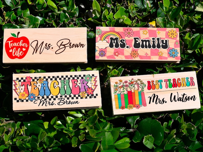 K&ouml;nnte beinhalten: Vier Namensschilder f&uuml;r Lehrer aus Holz mit verschiedenen Designs. Eines hat einen roten Apfel und die Worte "Teacher life" und "Mrs. Brown". Ein anderes zeigt einen Regenbogen und den Namen "Ms. Emily". Das dritte sagt "Teacher Mrs. Brown". Das letzte sagt "Best Teacher Mrs. Watson".
