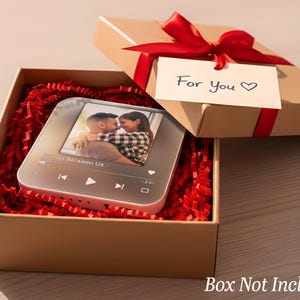 May include: A gift box with a red ribbon and a tag that says "For You". Inside, a personalized music player displays a photo of a couple. The box is filled with red paper shreds, creating a romantic presentation.