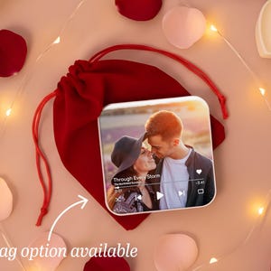 May include: A square photo print featuring a couple, displayed on a red velvet bag. The image is surrounded by rose petals, heart-shaped candles, and fairy lights. Text on the print reads "Through Every Storm".