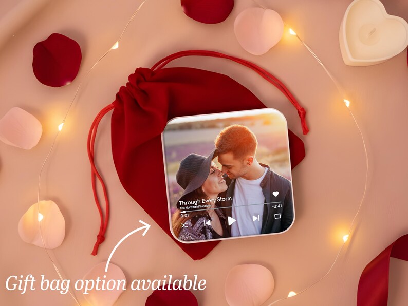 May include: A square photo print featuring a couple, displayed on a red velvet bag. The image is surrounded by rose petals, heart-shaped candles, and fairy lights. Text on the print reads "Through Every Storm".
