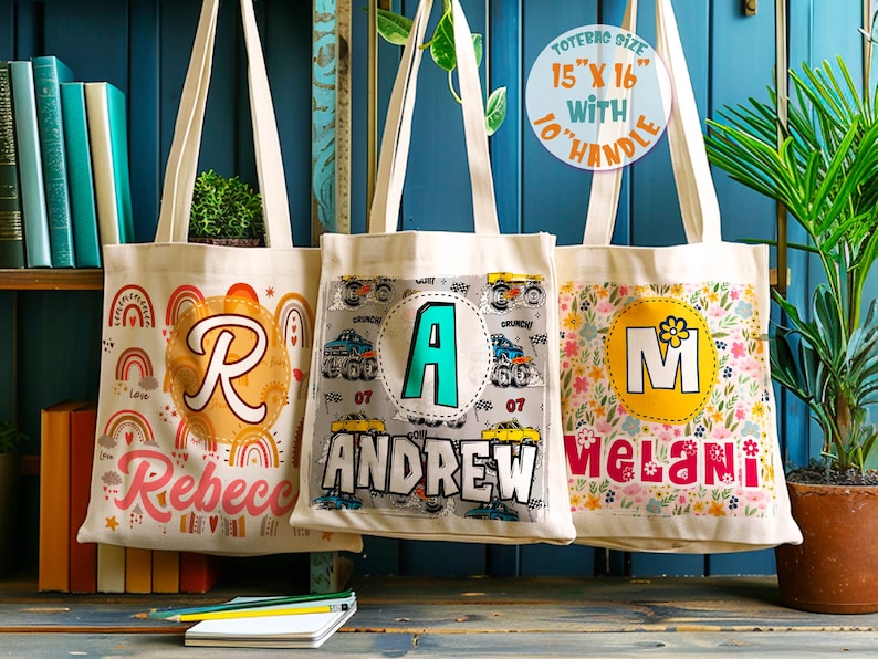 K&ouml;nnte beinhalten: Drei personalisierte Tragetaschen mit verschiedenen Designs. Die erste Tasche hat ein Regenbogen- und Herzdesign mit dem Buchstaben "R" und dem Namen "Rebecca". Die zweite Tasche hat ein Monstertruck-Design mit dem Buchstaben "A" und dem Namen "Andrew". Die dritte Tasche hat ein Blumendesign mit dem Buchstaben "M" und dem Namen "Melani". Die Taschen sind 38 cm x 41 cm gro&szlig; und haben 25 cm lange Griffe.