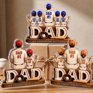 May include: Three custom acrylic baseball-themed displays featuring a central figure in a jersey labeled DAD #1, surrounded by smaller figures in jerseys with names and numbers. The base features the text DAD and WE CAUGHT THE BEST DAD.
