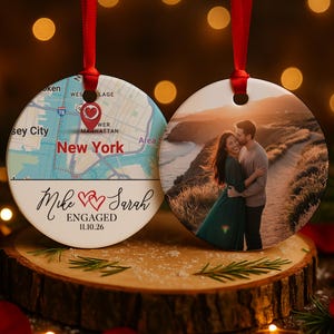 May include: Two round Christmas ornaments with red ribbons. One features a map of New York with a heart marking a location, the text "Mike & Sarah ENGAGED 11.10.26". The other shows a couple embracing at sunset.
