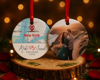 May include: Two round Christmas ornaments with red ribbons. One features a map of New York with a heart marking a location, the text "Mike & Sarah ENGAGED 11.10.26". The other shows a couple embracing at sunset.