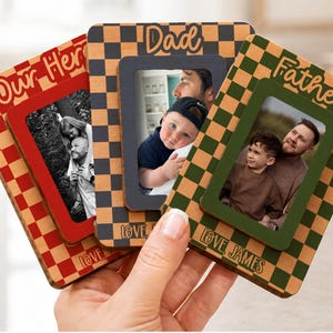 May include: Three wooden photo frames with checkerboard patterns and the words "Our Hero", "Dad", and "Father". Each frame holds a photograph and the words "Love James" are visible on one frame.