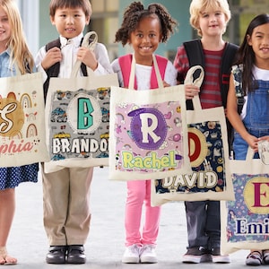 K&ouml;nnte beinhalten: F&uuml;nf personalisierte Tragetaschen mit verschiedenen Designs und Namen. Die Taschen sind wei&szlig; mit bunten Designs und die Namen "Sophia", "Brando", "Rachel", "David" und "Emily" sind darauf gedruckt.