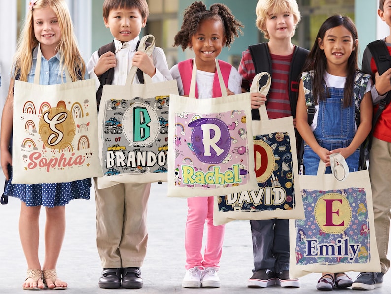 K&ouml;nnte beinhalten: F&uuml;nf personalisierte Tragetaschen mit verschiedenen Designs und Namen. Die Taschen sind wei&szlig; mit bunten Designs und die Namen "Sophia", "Brando", "Rachel", "David" und "Emily" sind darauf gedruckt.