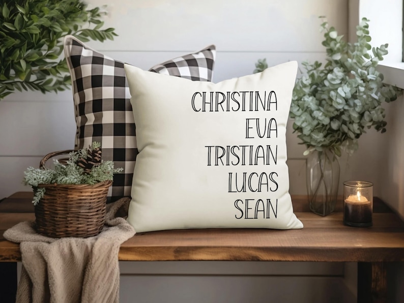May include: White pillow with black text that reads "Christina, Eva, Tristian, Lucas, Sean". The pillow is on a wooden surface with a black and white checkered pillow behind it.