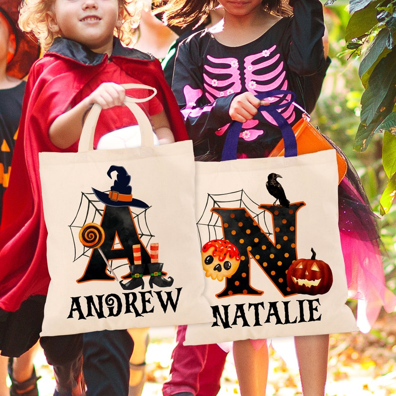 May include: Two white canvas tote bags with black handles. The bags feature a Halloween theme with spiderwebs, sweets, and a witch's hat. The bags are personalised with the names "Andrew" and "Natalie".