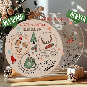 May include: Two round wooden signs with a Christmas theme. The sign on the left is made of plywood and has a brown background with white text and illustrations. The sign on the right is made of acrylic and has a clear background with white text and illustrations. Both signs have the text "a little Christmas treat for Santa".