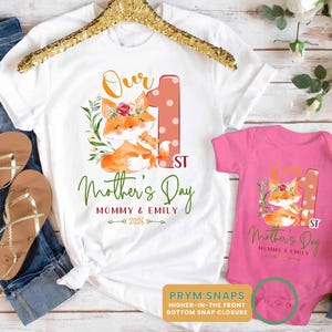 Puede incluir: Camiseta blanca y body rosa con un gr&aacute;fico de zorro a juego y texto para el D&iacute;a de la Madre. La camiseta y el body tienen el texto "Our 1st Mother's Day" y "Mommy & Emily 2026". El body tiene cierres de presi&oacute;n.