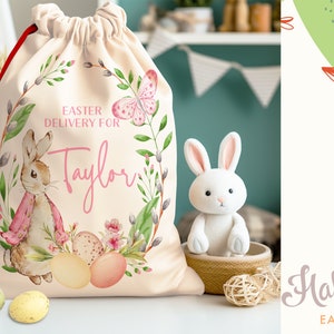 Pu&ograve; includere: Una borsa beige con coulisse con un design a corona di fiori che presenta un coniglio, farfalle e il testo "Easter Delivery for Taylor".