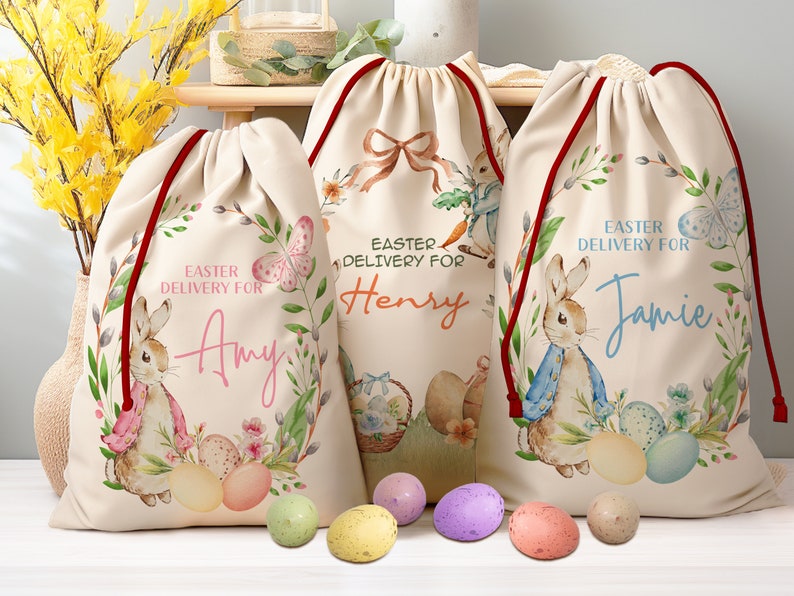 Pu&ograve; includere: Tre sacchetti regalo di Pasqua personalizzati con un design a coniglio e il testo "Consegna di Pasqua per" seguito da un nome. Le borse sono beige con laccetti rossi e presentano una ghirlanda di fiori con farfalle. I nomi sulle borse sono Amy, Henry e Jamie. Ci sono anche diverse uova di Pasqua colorate nell'immagine.