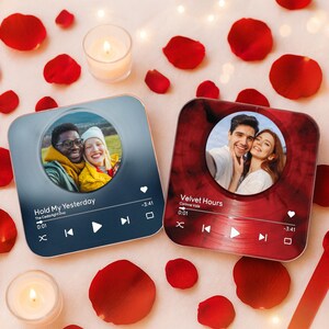 May include: Two square coasters with photos of couples, designed to look like music players, are surrounded by red rose petals and candles. One coaster is blue with the text "Hold My Yesterday". The other is red with the text "Velvet Hours".