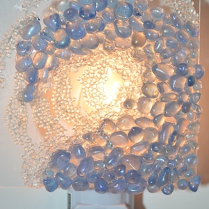 May include: A white night light with a clear glass shade. The shade is decorated with blue and clear glass beads in a wave pattern.