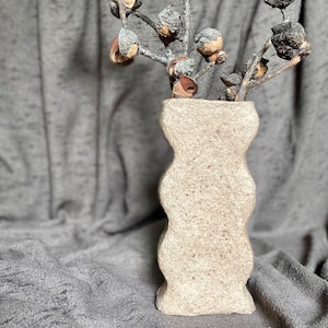 May include: A white ceramic vase with a textured, wavy design. The vase is empty and has a light brown colour.