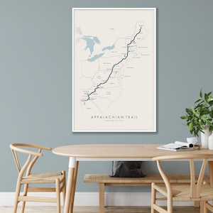 May include: A beige map print with a dark blue line tracing the Appalachian Trail across the United States. The map is framed in a white frame and hanging on a light blue wall.