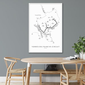 May include: A black and white map of Torres del Paine National Park in Chile, showing the W-Circuit hiking trail. The map is framed in a white frame and hanging on a gray wall.