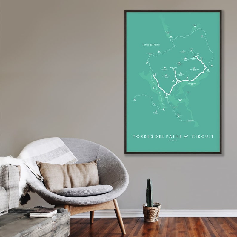 May include: A turquoise and white map of Torres del Paine National Park in Chile, showing the W-Circuit hiking trail. The map is framed in black and hanging on a wall.