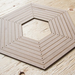 May include: A collection of nested, hexagonal wooden frames. The frames are constructed from light brown wood and diminish in size towards the centre. Small holes are drilled along the edges of each frame. The frames are arranged on a light wood surface.