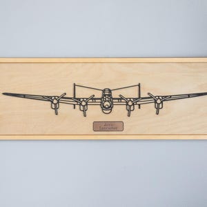 Könnte beinhalten: Wandkunst aus Holz mit einer schwarzen Umrisszeichnung eines Avro Lancaster Bombers. Das Kunstwerk ist auf einer hellen Holzplatte mit rechteckigem Rahmen montiert. Ein kleines Schild trägt die Aufschrift "Avro Lancaster".