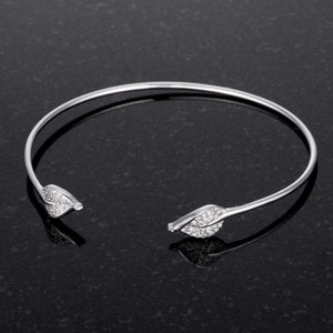 May include: A silver bangle bracelet with two leaf-shaped ends that are encrusted with clear cubic zirconia stones.