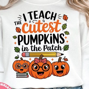 Peut inclure: Sweat-shirt blanc avec l'inscription "I teach the cutest pumpkins in the patch" et trois citrouilles de dessin animé. Les citrouilles ont des lunettes, des nœuds et des visages souriants. Un crayon et des feuilles sont également présents.