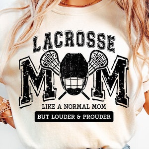 Puede incluir: Una camiseta blanca con un gráfico negro que dice "Lacrosse Mom" con un palo de lacrosse y un casco. El texto debajo del gráfico dice "Como una madre normal pero más fuerte y más orgullosa".