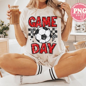 May include: A white t-shirt with red glitter text that says "GAME DAY" and a black and white soccer ball graphic.