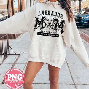 May include: A white hoodie with a black graphic design that says "Labrador Mom" with a picture of a Labrador Retriever. The text below the graphic says "Like a normal mom except much cooler."