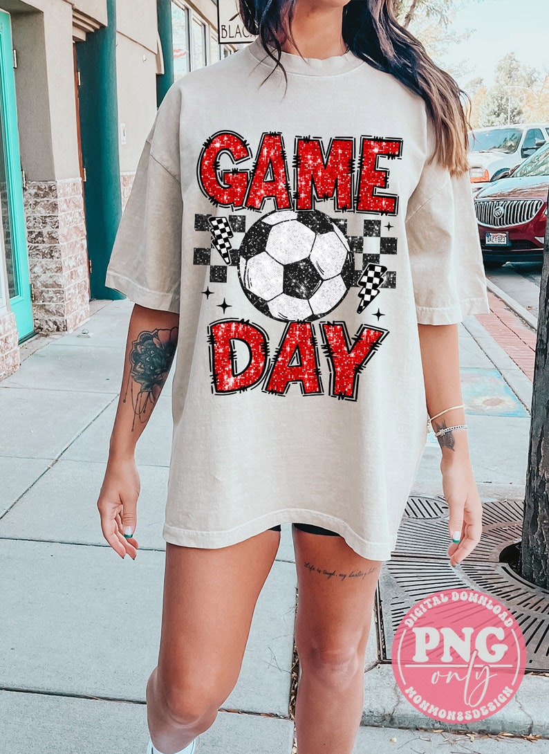 May include: A white t-shirt with a red glitter graphic that says "GAME DAY" with a soccer ball and checkered flags.