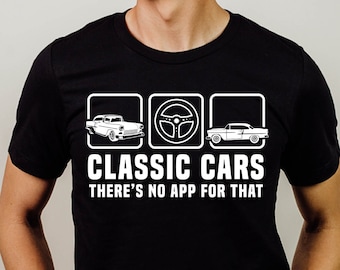 May include: A black t-shirt with a white graphic design featuring three icons: a classic car, a steering wheel, and another classic car. The text "CLASSIC CARS THERE'S NO APP FOR THAT" is printed below the icons.