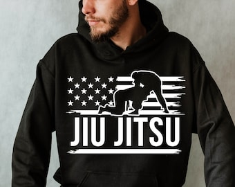 May include: Black hooded sweatshirt with a white graphic of a jiu-jitsu match and the text "JIU JITSU" on a distressed American flag background.
