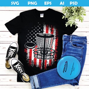 以下が含まれることがあります： アメリカ国旗のデザインが施された黒いTシャツ。Tシャツには、ディスクゴルフのバスケットが描かれている。バスケットは黒で、国旗は赤、白、青である。
