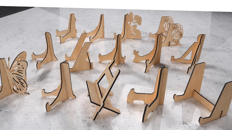 May include: A collection of wooden display stands in various designs. Some stands feature cut-out butterfly, floral, and geometric patterns. The stands are made of light-colored wood with dark edges and are suitable for displaying items.