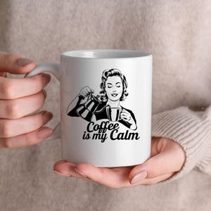 May include: White ceramic mug with a black and white illustration of a woman pouring coffee. The text "Coffee is my Calm" is printed on the mug.