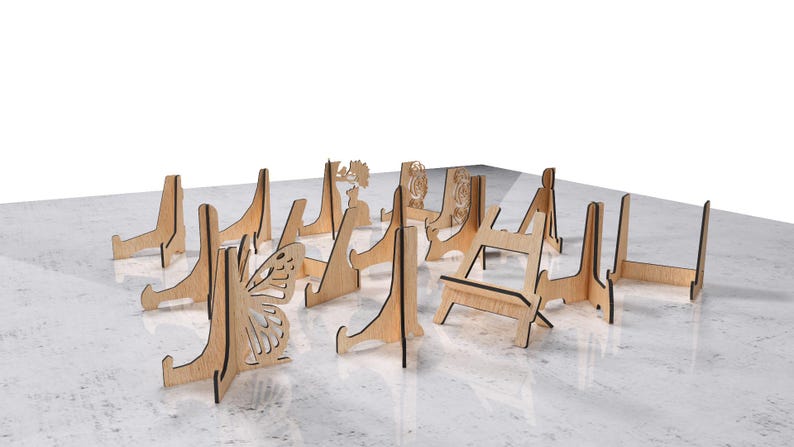 May include: A collection of wooden display stands in various designs, including a butterfly, floral, and geometric patterns. The stands are made of light-colored wood and are arranged on a light-colored surface.