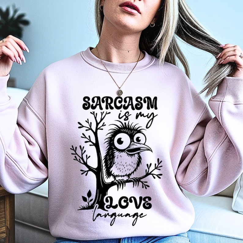 Może przedstawiać: Jasnor&oacute;żowa bluza z napisem "Sarcasm is my Love Language" i rysunkiem ptaka siedzącego na gałęzi. Ptak ma duże oczy i dzi&oacute;b. Tekst i ptak są czarne.