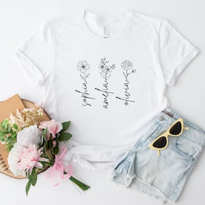 May include: White t-shirt with a floral design and the names "Sophia", "Amelia", and "Olivia" written vertically.