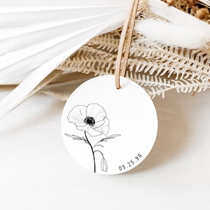 May include: A white round tag with a black line drawing of a poppy flower and the date 05.25.90.