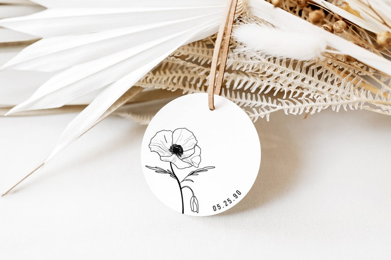May include: A white round tag with a black line drawing of a poppy flower and the date 05.25.90.